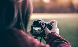 Girl, taking a photo with the camera, on the beautiful meadow in colorful and beautiful light