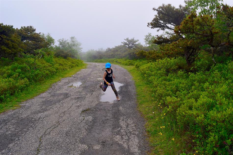 Girl running on the road, with the water puddles, among the beautiful and colorful plants