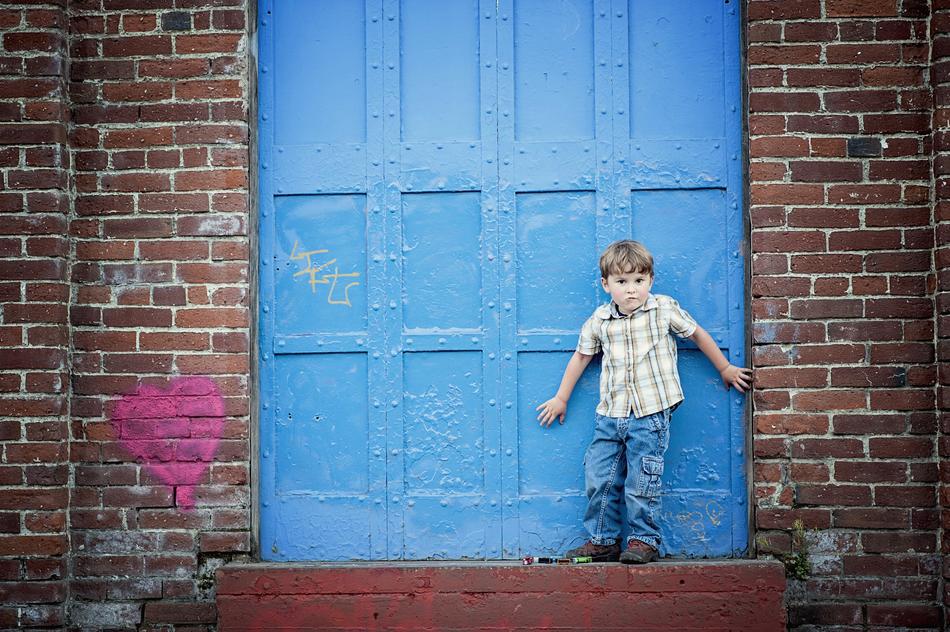 Child boy, standing near the blue door of the brick building