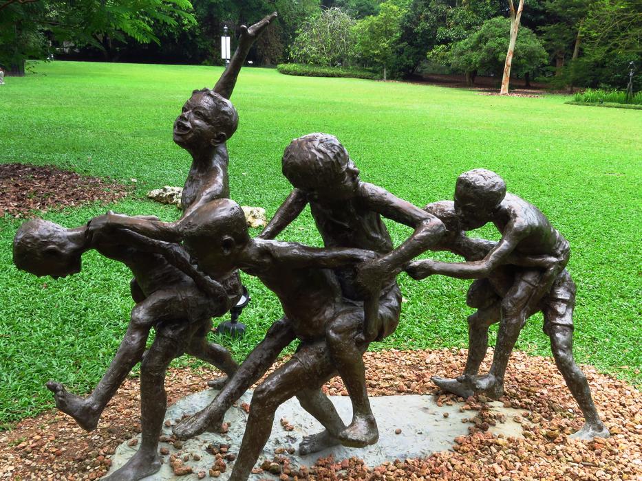 Statue of the playing children, near the green meadow, among the green trees