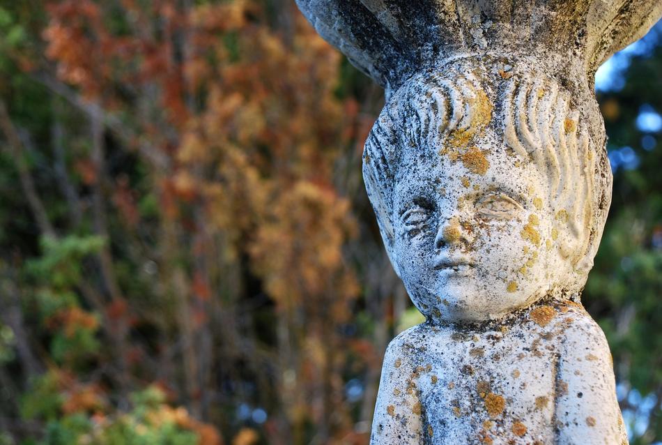 Colorful source statue of the child, in the park, in light, among the colorful plants