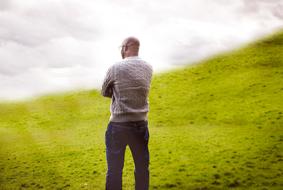 a man stands with his back on green grass against a background of clouds