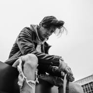 Black and white photo of the guy in ripped jeans, sitting near the building