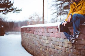 man with a book sits on a brick wall