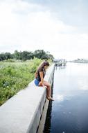 Girl, sitting on the beautiful shore of the canal, with green plants