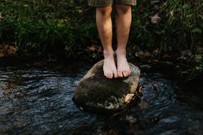 Child feet on stone in river