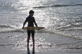 boy with skimboard near the sea at sunset