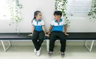 Students, sitting on the bench, in the international school, near the windows with green plants