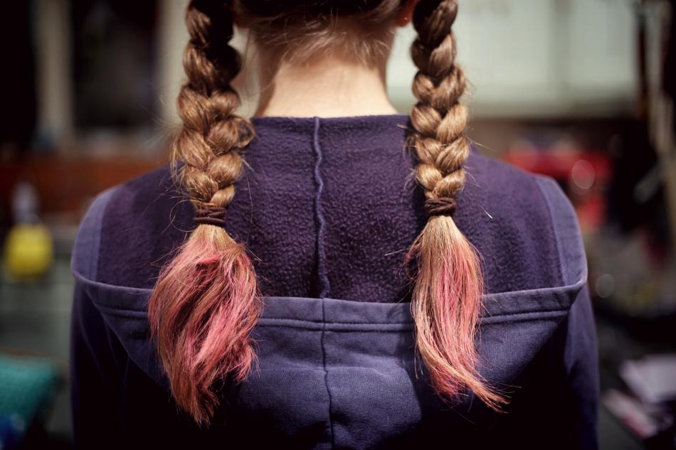 Back view of the girl, with the colorful braids, at blurred background