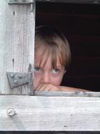 serious caucasian child looking from wooden window