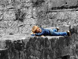 Child boy, lying on the grey rocks