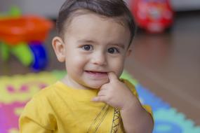 Portrait of the smiling child, wit the finger in the mouth, on the playground in the house