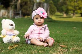 Cute girl child, with the colorful and beautiful flowers and Teddy Bear, sitting on the green grass, among the colorful plants