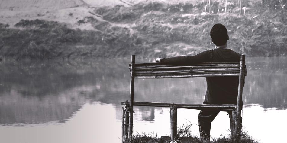 monochrome photo of a man on a bench by the river