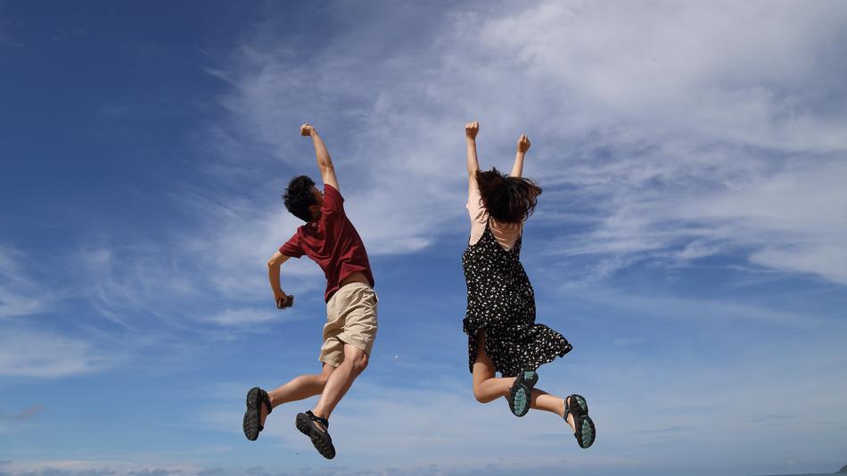 Jumping man and woman at blue sky with white clouds on background