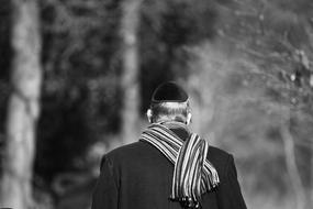 Black and white photo, with the back view of the Jewish man, in the Kippah, near the trees