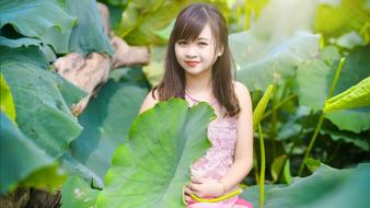 Smiling Asian girl in colorful dress, among the colorful plants with the big leaves, in sunlight