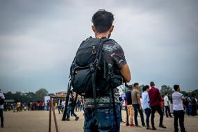 Back view of the man, with the backpack, near the other people, on the sand