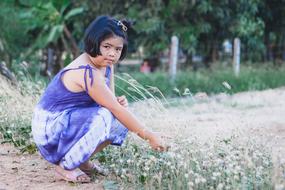 Sitting, young girl on the colorful plants, near the green plants