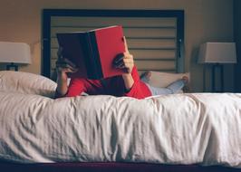 Person, reading red book, while laying on the bed