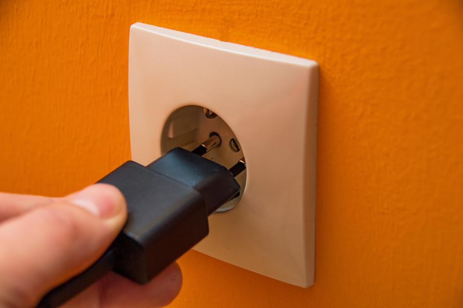 Person, plugging black plug in the white socket, in the orange wall
