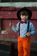 a boy in a hat and orange pants stands near a retro radio