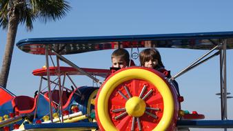 Kids, on the colorful, shiny plane, near the palm tree, on the carnival, outdoors
