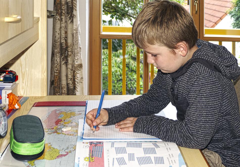 Profile portrait of the sitting boy, doing homework at the desk