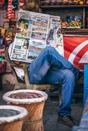 Person reading newspaper on the chair, near the colorful market