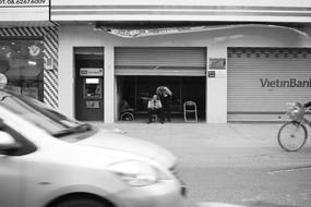 Black and white photo with the car near the man, bike and buildings