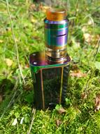 Close-up of the beautiful and colorful, shiny "Ijoy Captain" vape, on the green grass with colorful leaves