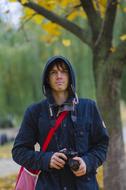 Portrait of the guy with the camera, covered in hood, among the plants