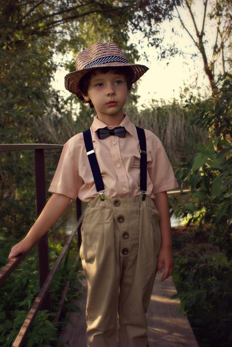 Boy in costume, with the bow tie and hat, on the bridge among the plants