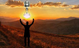 Silhouette of the person, with the colorful light bulb, on the mountains, at colorful and beautiful sunset
