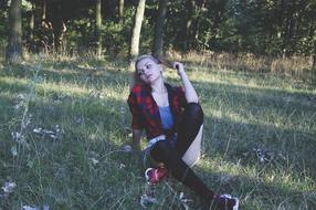 Girl sitting posing on the grass near the trees of the forest