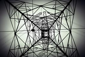 Black and white low angle shot of the steel electricity tower, under the cloudy sky