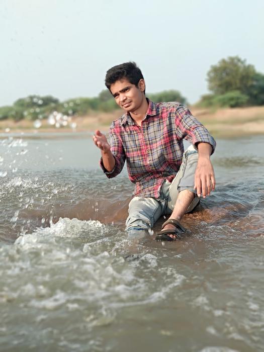 Guy posing in the water, near the sand and green plants on the coast
