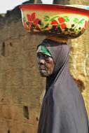 Profile portrait of the woman in traditional wear, holding colorful bowl with patterns on the head