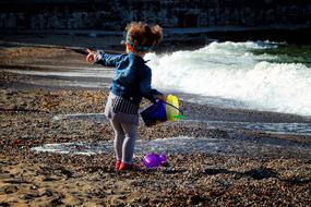 Girl playing with the colorful toys on the sandy beach with waves