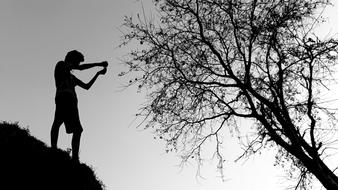 Black and white photo with silhouette of the person on the hill, near the tree