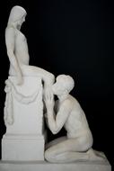 Sculpture with the man kissing woman's leg, at black background