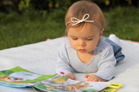 Cute, little girl looking at the collection of short stories for children, among the plants