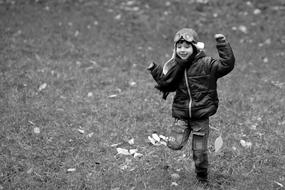 Black and white photo of the smiling boy in helmet, running in the forest, in the autumn