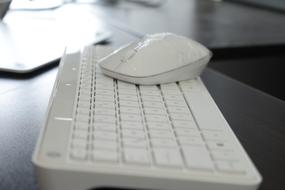 Close-up of the shiny, white mouse on the shiny, white keyboard, on the desk in light