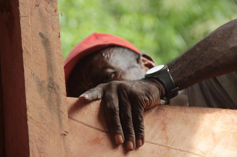 Man in red cap and with wrist watch, hiding behind the wooden construction