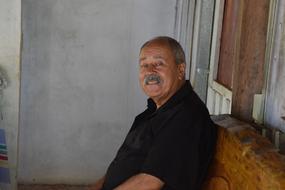 Portrait of the smiling man with moustache, sitting on the wooden bench