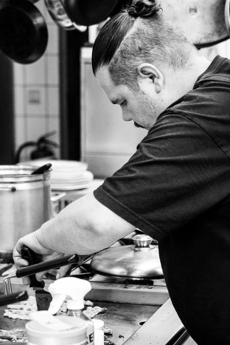 black and white, a man fries in a skillet in the kitchen