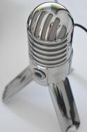 Close-up of the shiny, chrome microphone, with the wire, with the shadow on the white surface