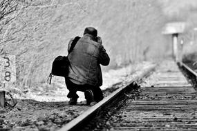 Black and white photo with back view of the photographer man near the disused railway line, among the plants