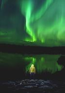 man by the sea looks at the green northern lights